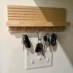 several keys hanging from hooks on a wall with a wooden shelf above it and below them is a light switch