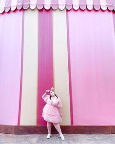 a woman standing in front of a pink and white striped wall with her arms behind her head