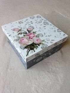 a white box with pink roses on it sitting on top of a tablecloth covered surface