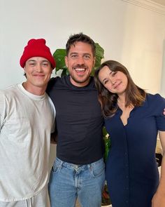 three people standing next to each other in front of a potted plant and smiling at the camera