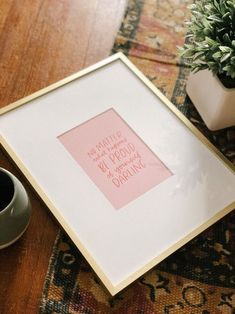 there is a framed pink note on the floor next to a cup and plant in front of it