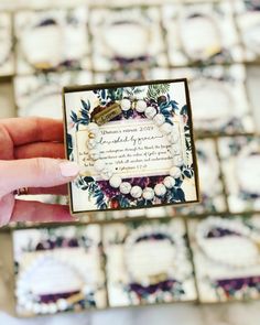 a person holding up a small card in front of some plates with flowers on them