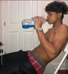 a shirtless man sitting in a chair drinking from a water bottle