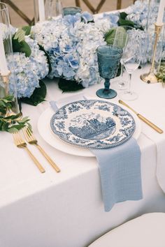 a table set with blue and white plates, silverware and flowers on the table