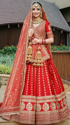 a woman in a red and gold bridal gown posing for the camera with her hands on her hips