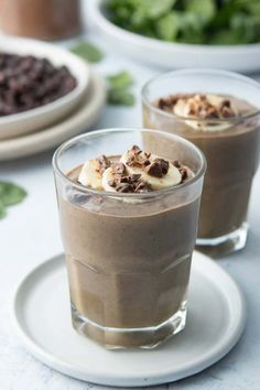 two glasses filled with chocolate pudding on top of a white plate next to other desserts