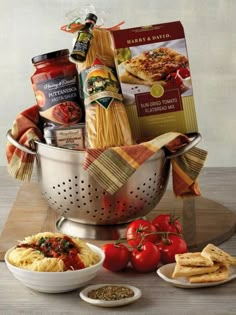 a large metal colander filled with pasta, tomatoes and other food items sitting on a wooden table