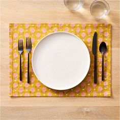 a place setting with black and white utensils on a yellow patterned place mat