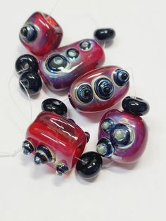 five red and black glass beads on a white surface with wires in the middle one bead has an oval hole at the center