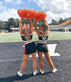 two cheerleaders in black and orange outfits holding pom poms on their heads