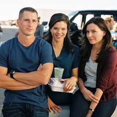 three people sitting next to each other in front of a truck with their arms crossed