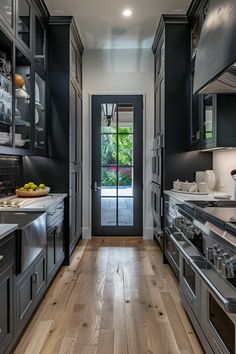 a long narrow kitchen with stainless steel appliances and black cabinets, along with hardwood flooring