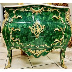 an ornate green and gold painted chest of drawers on tile flooring in front of mirrors