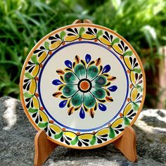 a colorful plate sitting on top of a wooden stand next to some plants and rocks