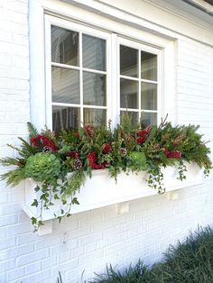 a window box with flowers and greenery on the side of a white brick building