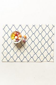 a bowl of fruit sitting on top of a white place mat next to a spoon