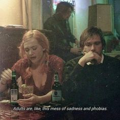 a man and woman sitting at a table with beer bottles in front of their faces