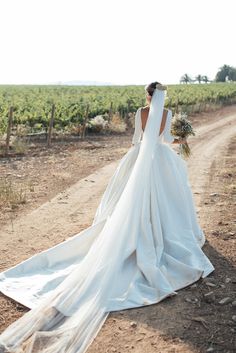 a woman in a wedding dress walking down a dirt road with her back to the camera