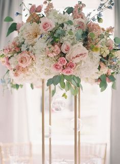 a tall vase filled with pink and white flowers on top of a table next to chairs