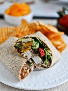 a burrito cut in half sitting on top of a white plate next to chips