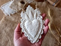 a hand holding a heart shaped ornament in front of some twine spools