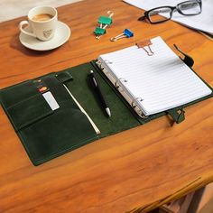 a desk with a notebook, pen and glasses on it next to a cup of coffee