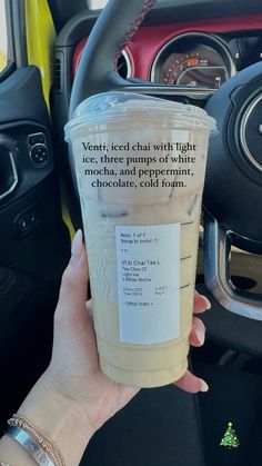 a woman holding up a cup of coffee in her car with the words ventri - iced chai with light ice, three pumps of white chocolate and