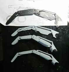 three knives are laying on top of a piece of paper with some drawings in the background