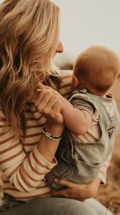 a woman holding a baby in her arms and looking at the camera while she is wearing a striped shirt