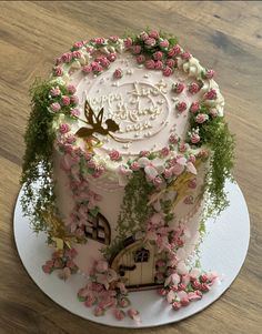 a cake decorated with pink flowers and greenery on a white plate sitting on a wooden table