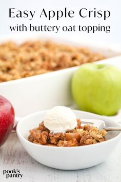 an apple crisp with buttery oat topping in a bowl next to two apples