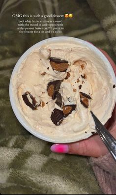 a hand holding a white bowl filled with ice cream and chocolate pieces on top of it