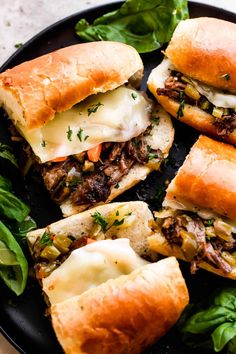 several sandwiches cut in half on top of a black plate with lettuce and cheese