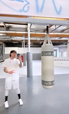 a man in white shirt and shorts standing next to a punching bag