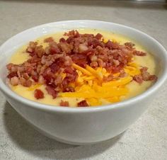 a white bowl filled with cheese and bacon on top of a counter next to a spoon