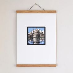 an art piece hangs on the wall above a white framed photograph with a reflection of a building