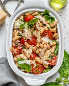 a white bowl filled with pasta salad and topped with tomatoes, spinach leaves and parmesan cheese