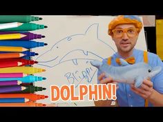 a man holding a stuffed dolphin in front of a whiteboard with colored crayons on it