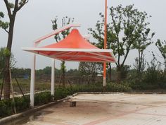 an orange and white tent sitting on top of a cement ground next to some trees