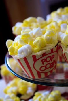 popcorn cupcakes with yellow and white frosting are on a clear cake plate