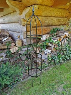 an iron birdcage stands in front of a pile of firewood and logs