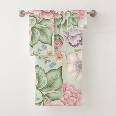 two towels hanging on a towel rack with flowers and leaves printed on them, along with a white wall