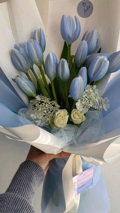 a bouquet of blue tulips and white roses is held by a woman's hand