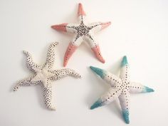 three starfishs are sitting on a white surface and one is pink, the other is blue