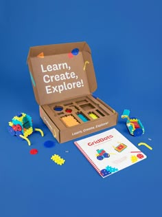 an open cardboard box filled with toys on top of a blue surface and the words learn, create, explore written in large letters