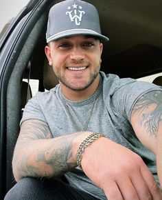 a man sitting in the back of a car wearing a hat and tattoos on his arm