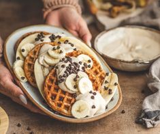 a person holding a plate with waffles topped with bananas and chocolate chips on it