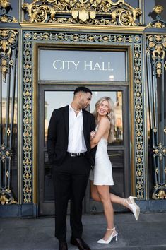 a man and woman are standing in front of a city hall entrance with their arms around each other