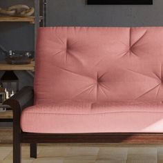 a pink futon sofa sitting on top of a hard wood floor next to a book shelf