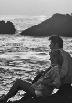 a man and woman are sitting on the rocks by the water with an ocean in the background